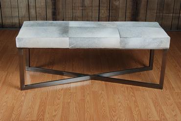 A rectangular bench with a grey leather top and a zinc metal frame, placed on a wooden floor.