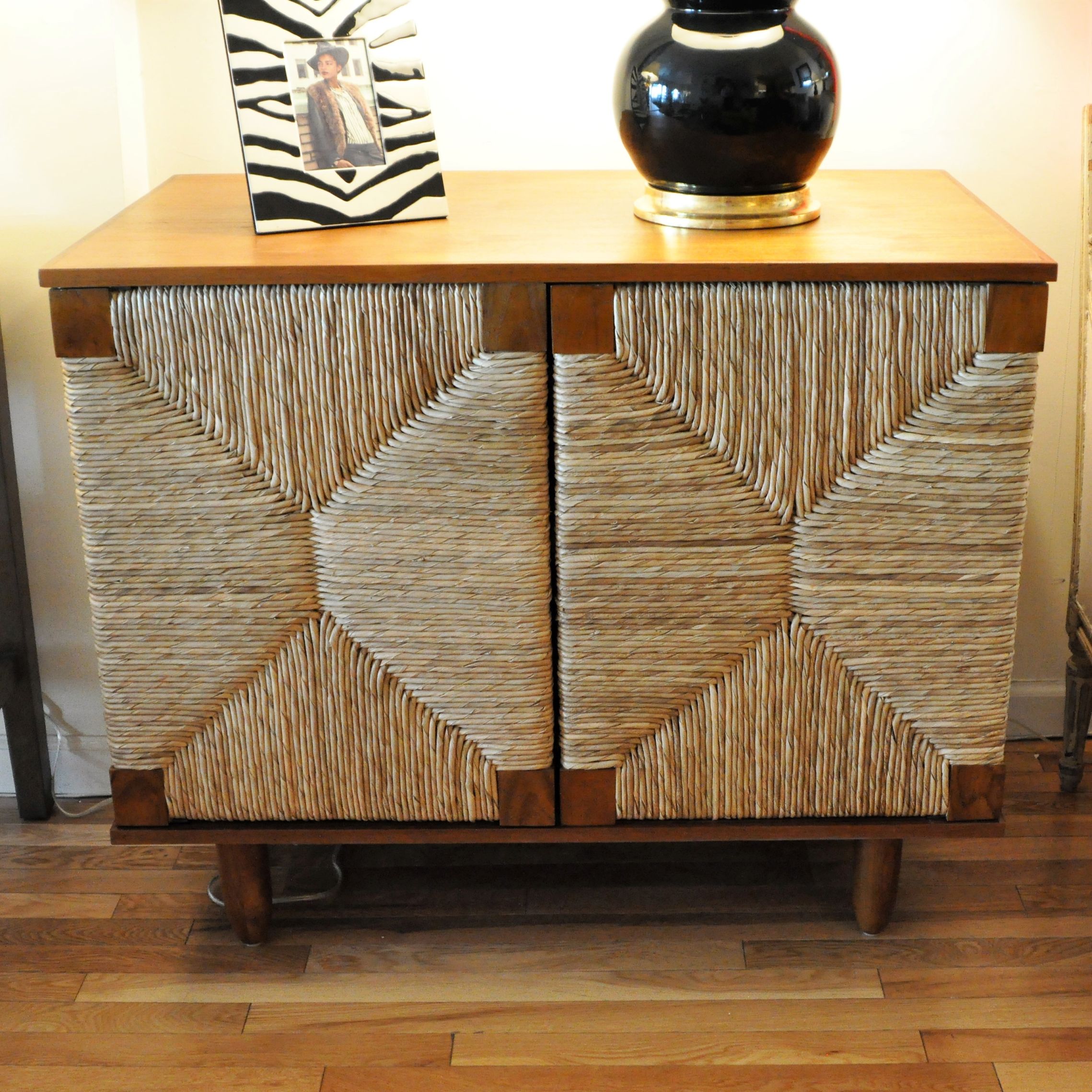 Small wooden buffet with woven front, featuring a dark brown finish and two doors, set against a white wall.