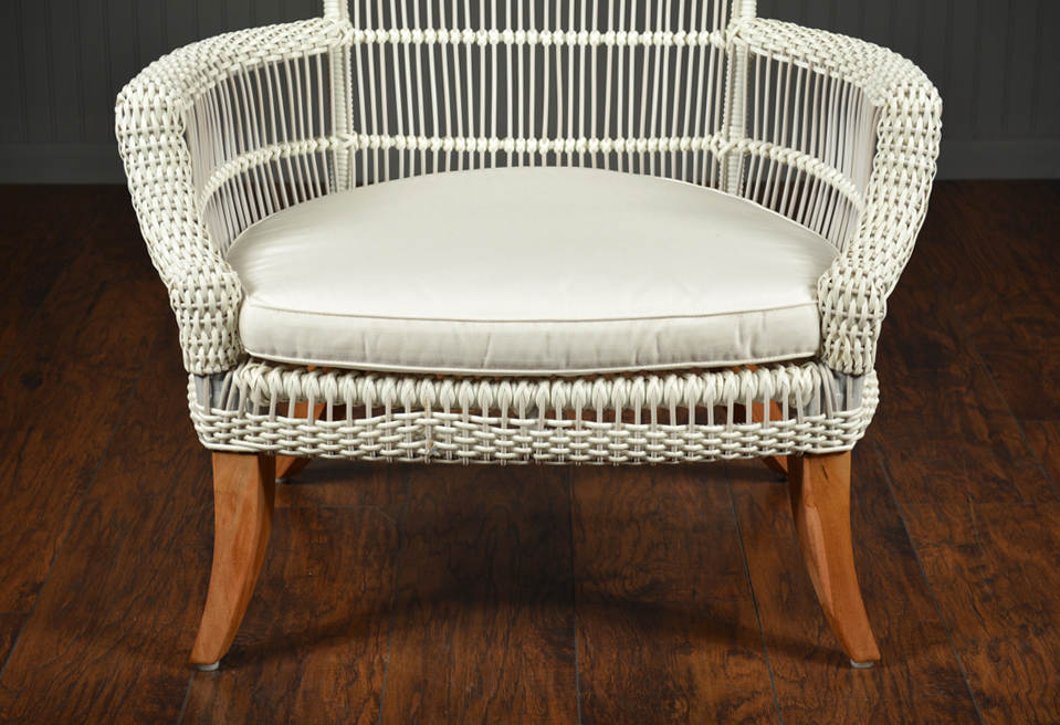 The image features a wicker chair with a white cushion and wooden legs, standing against a dark background.