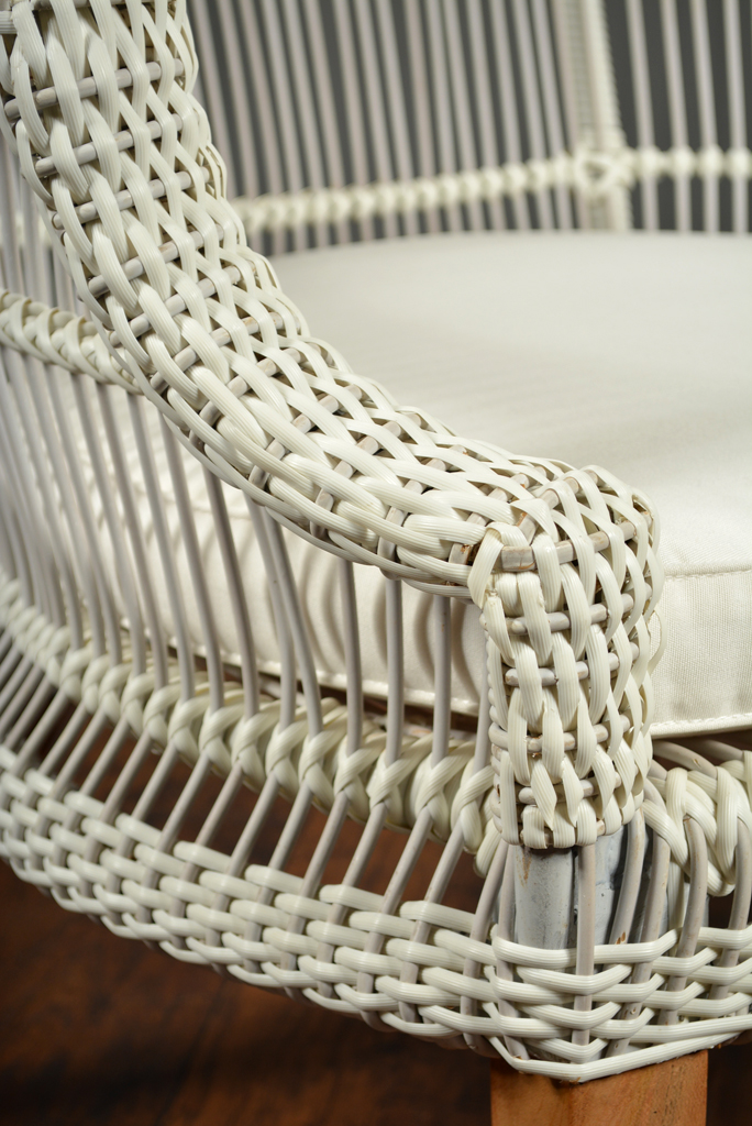 A wicker chair with a cushioned seat, featuring a braided design and teak legs, presented in a close-up shot.