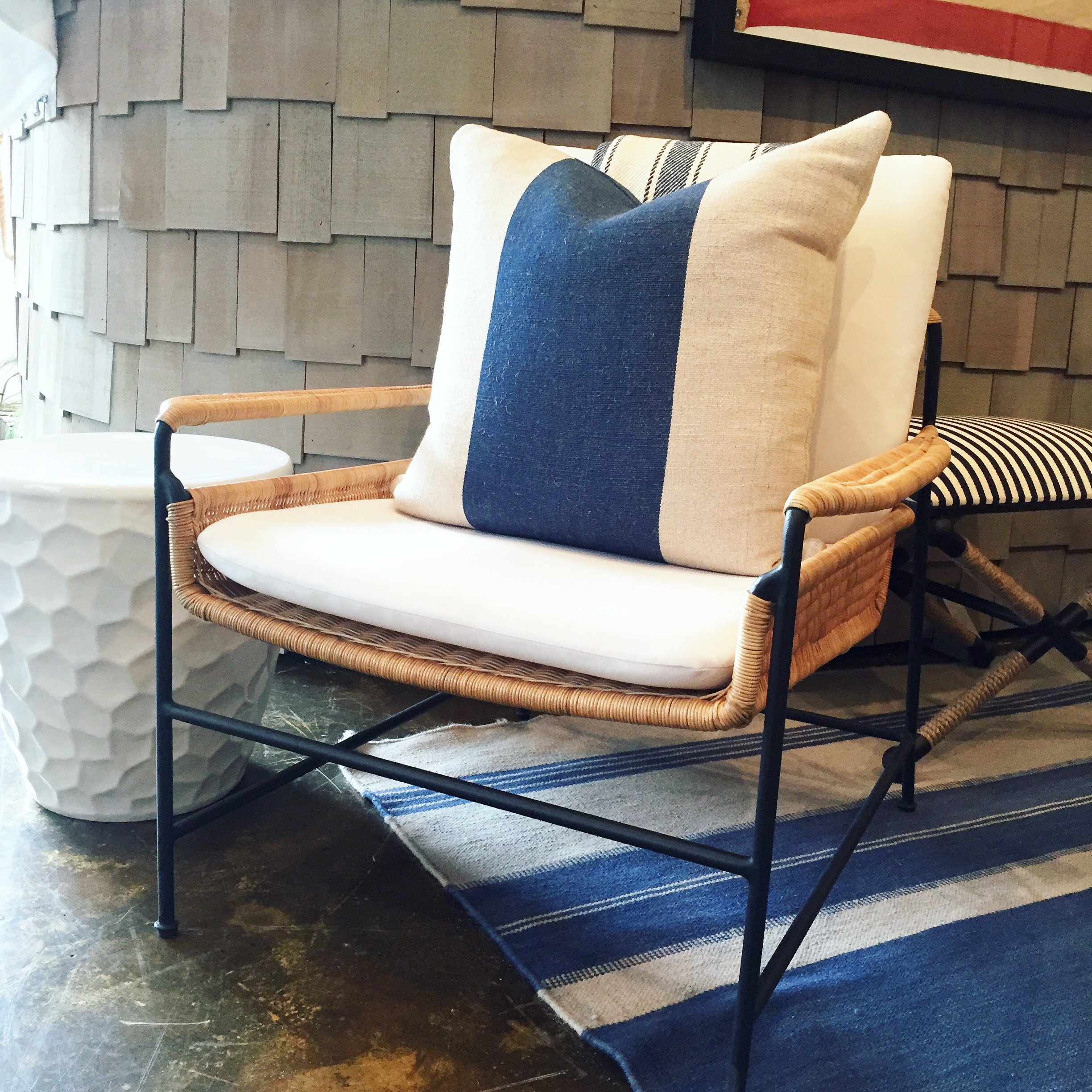 A wicker and metal club chair with a blue and white striped cushion in a cozy room setting.