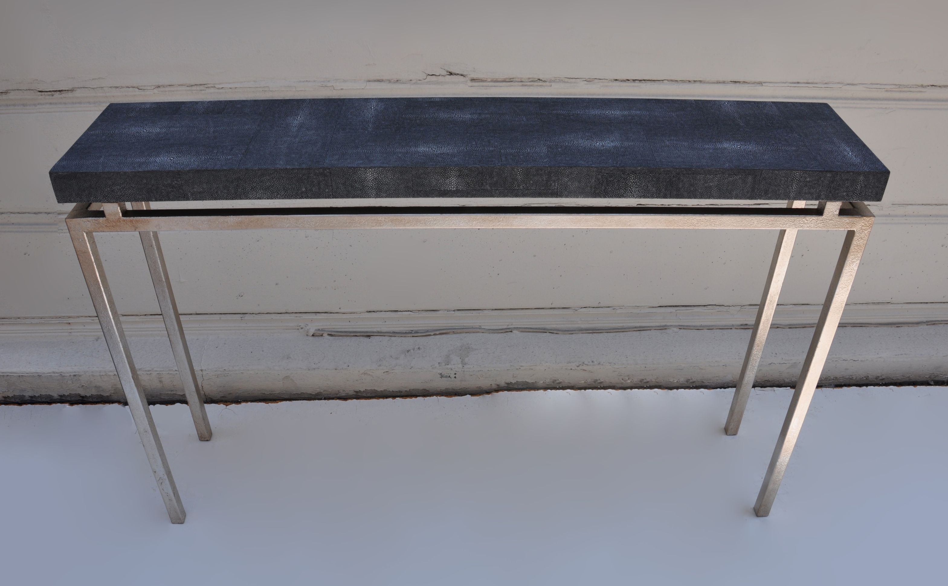 Black and silver console table with a black marble top, standing against a white wall.