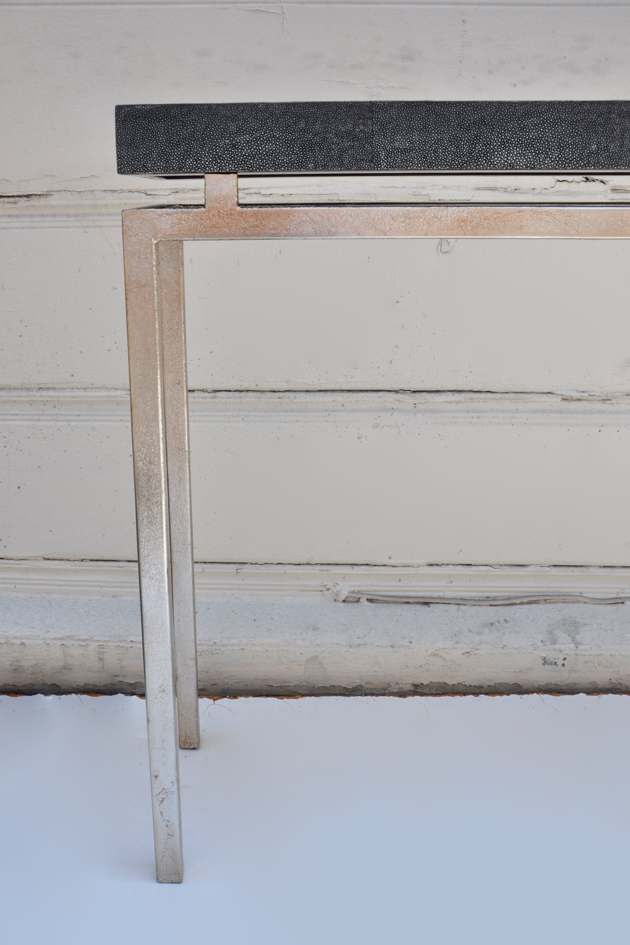 Small metal console table with a black top, standing against a white wall.