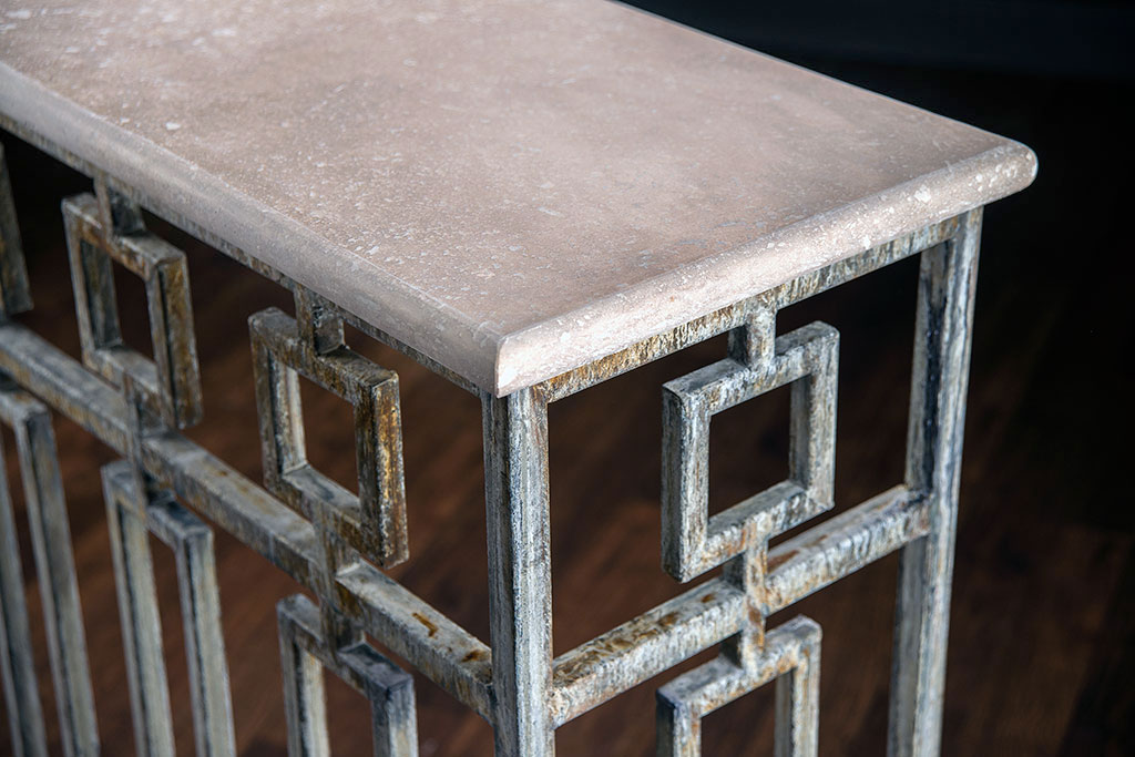 The image showcases a Hewitt Console with a light travertine top in a deep ocean finish It features a metal frame with