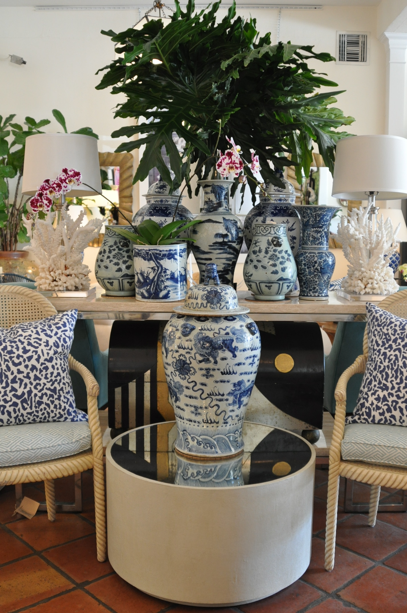 A faux shagreen mirrored coffee table in a room with blue and white patterned chairs potted plants and a vase with flowers