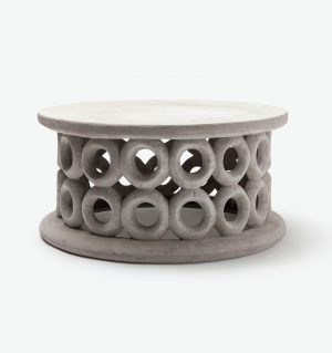 A decorative round outdoor coffee table with a natural stone finish featuring circular cutouts and a raised edge set against a neutral