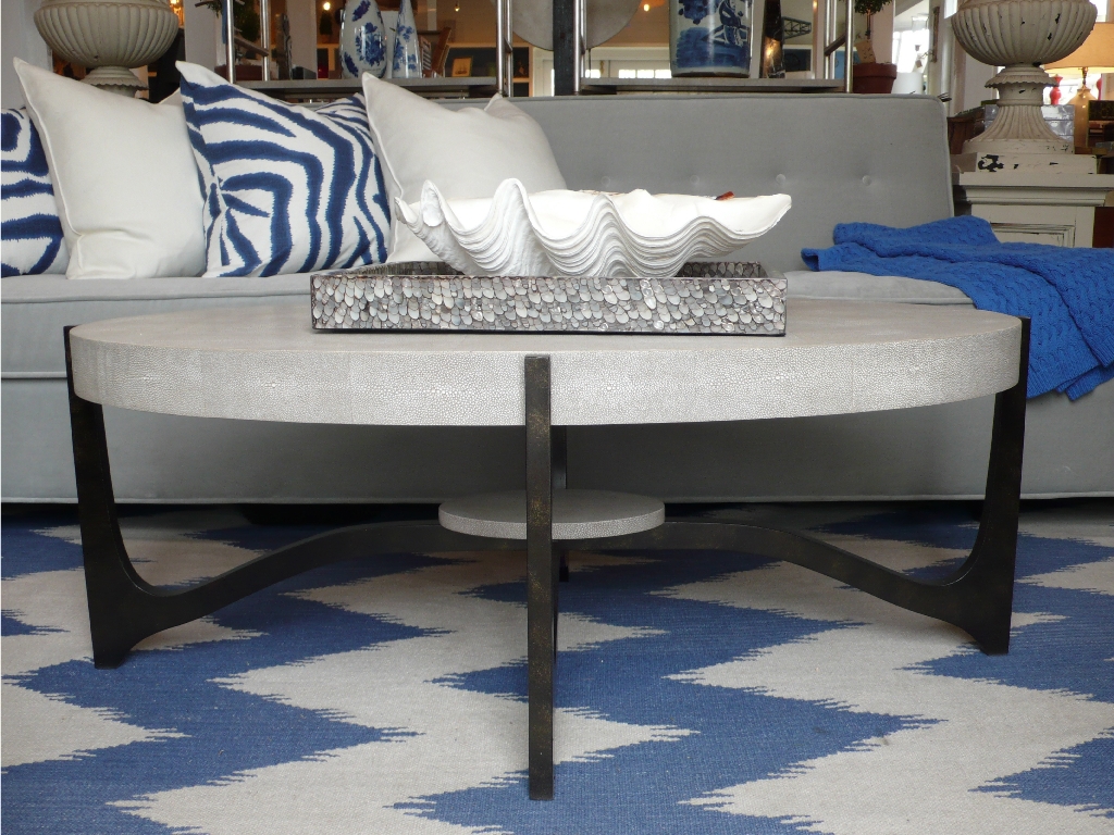 A modern coffee table with a glossy, oval top in a faux shagreen finish, set against a blue and white patterned rug.