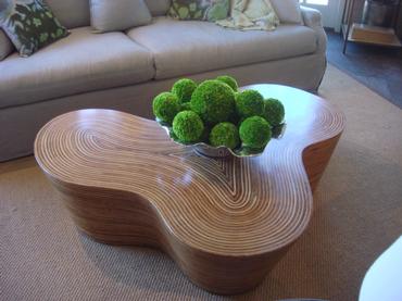 The image features a modern organic striped wood coffee table with a curved design set against a backdrop of a living room