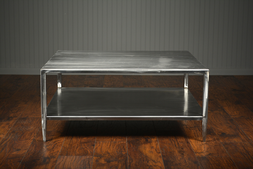Brushed steel coffee table with two levels and slightly tapered legs featuring an open bottom shelf set against a wooden floor in