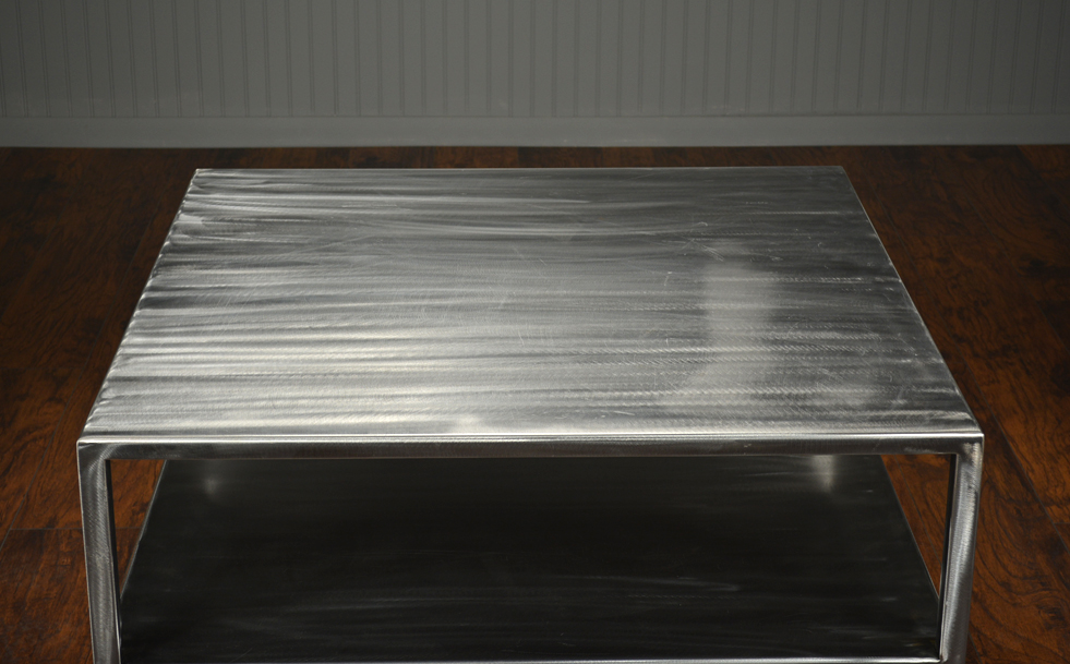 Brushed steel coffee table with two levels and slightly tapered legs featuring an open bottom shelf available in custom sizes and finishes