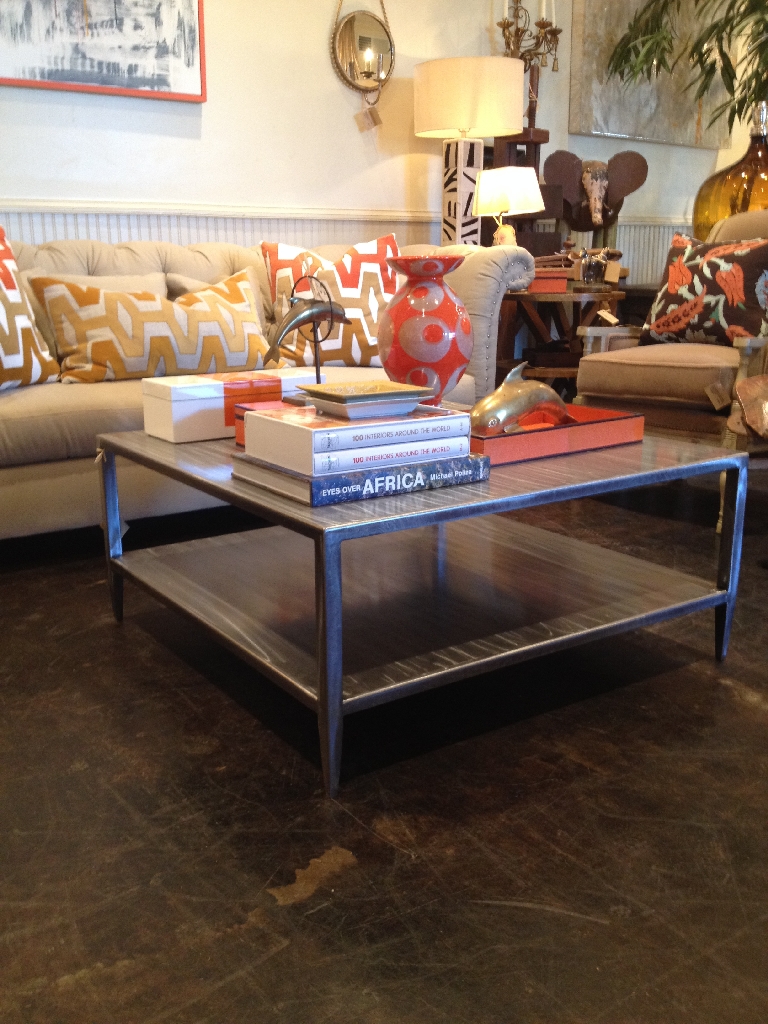 Brushed steel coffee table with two levels and slightly tapered legs sitting on a polished floor in a living room setting with