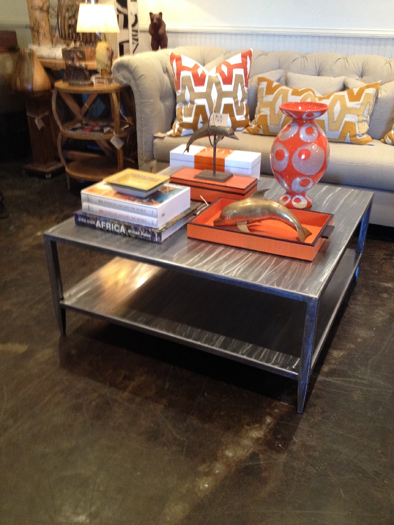 Brushed steel coffee table in a living room, with a vase and books on top.