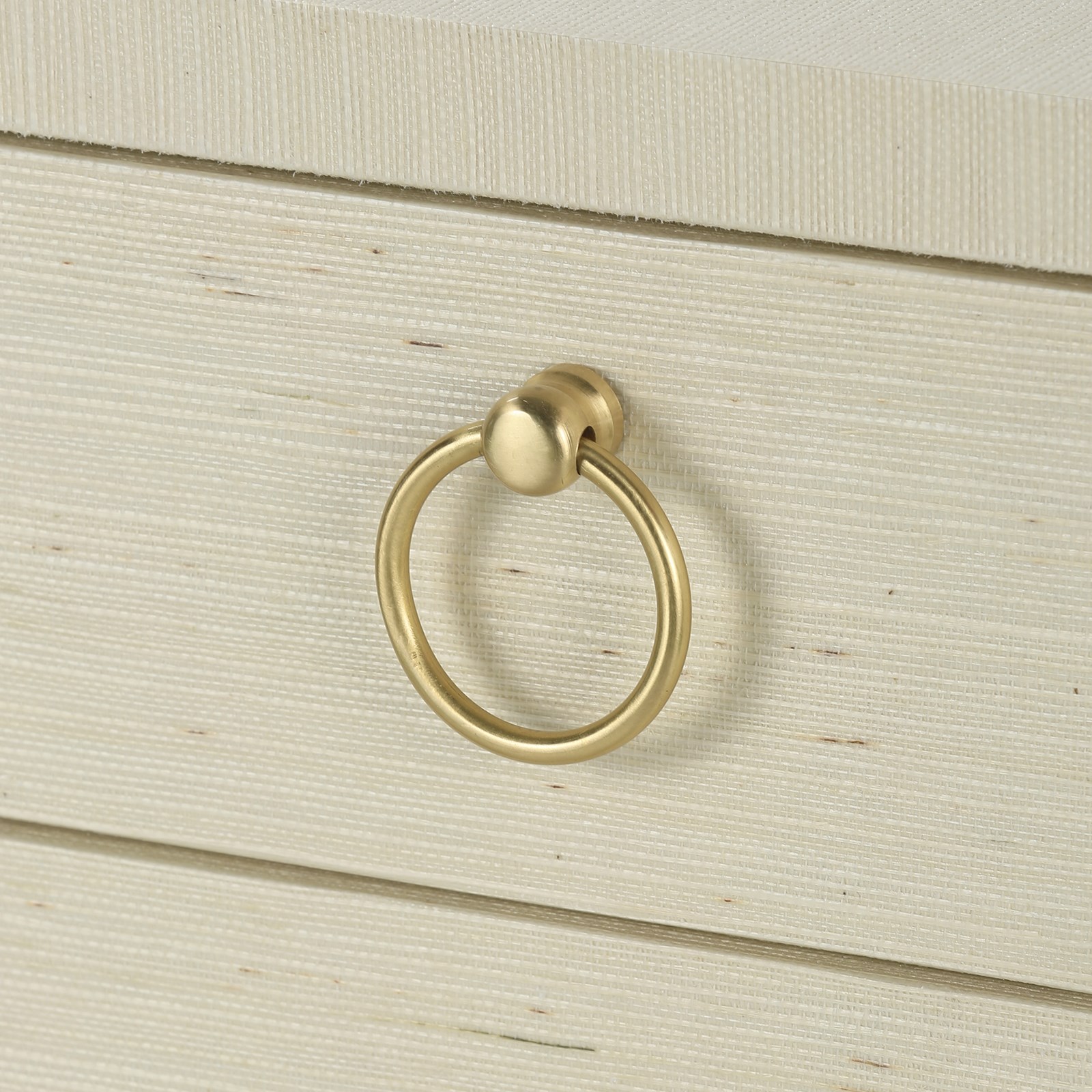 A brass ring pull on a white dresser with a natural finish and soft closing glides.