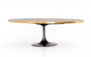 Grey iron tulip base dining table with burnt oak oval top and polished brass steel band featuring exposed nailhead detail.
