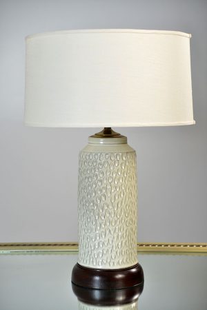 A creamy white handcrafted dimpled tea jar ceramic lamp with a wooden base and drum shade, set against a plain background.