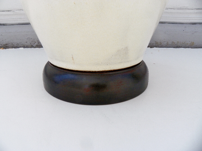 A glazed ceramic egg lamp with a matte white finish and a thick wood base, set against a snowy background.