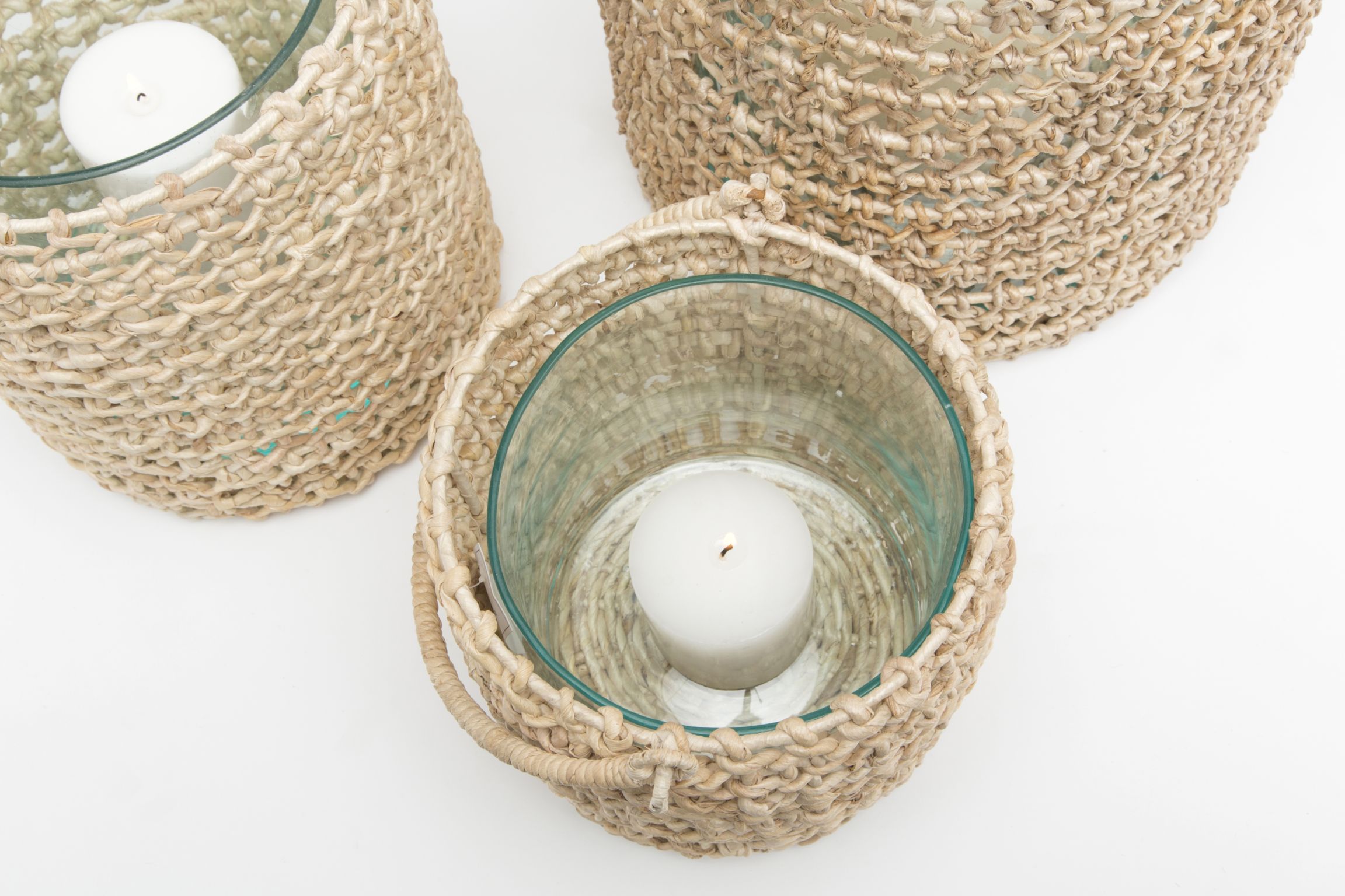 A collection of woven banana bark hurricanes in various sizes, with clear glass inserts and a candle inside one of them.
