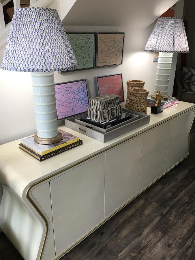 A long curved wooden table with a white marble top and two matching lamps on either end The lamps have open weave