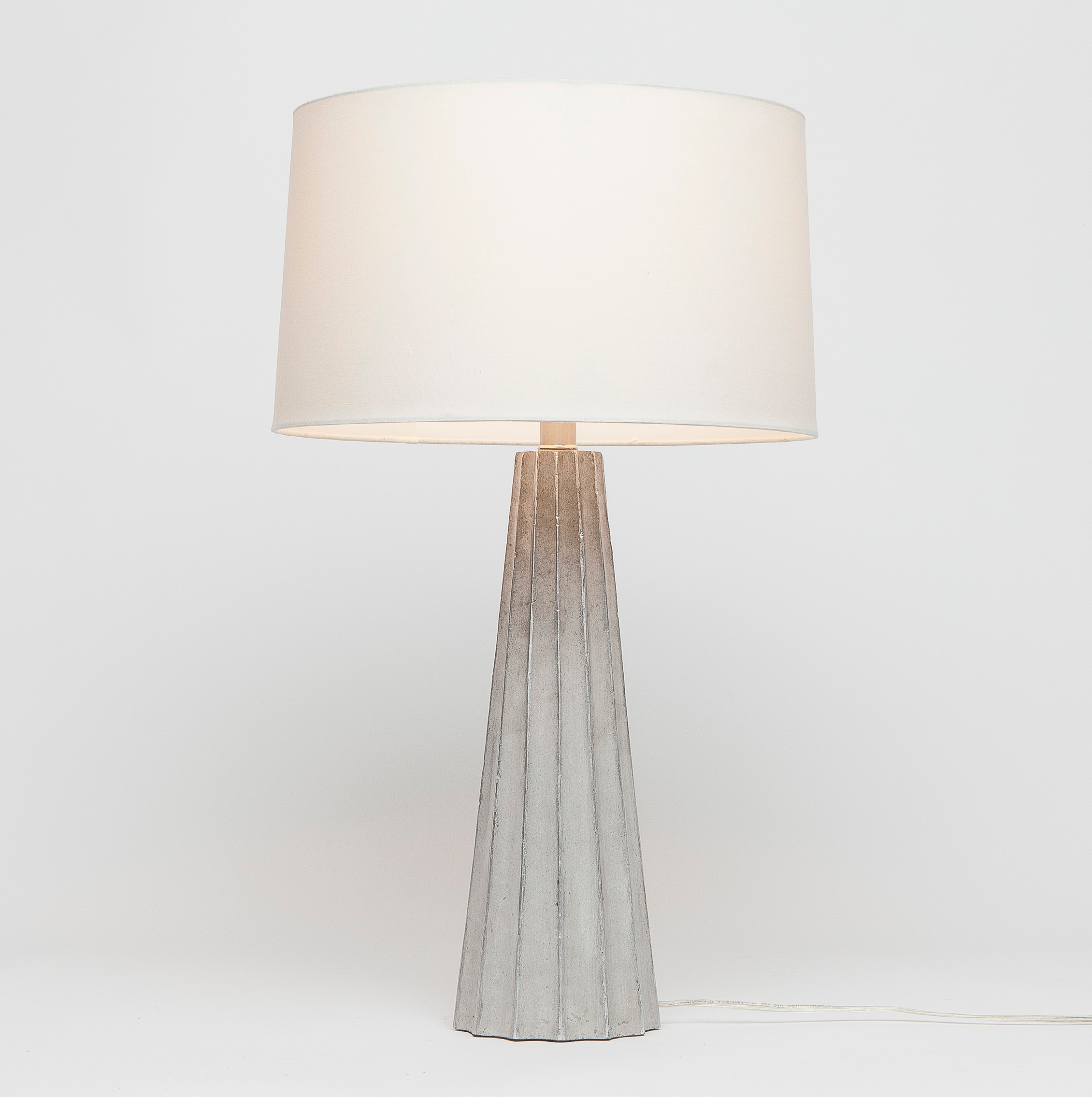 A modern table lamp with a cylindrical base featuring a fluted design and a metallic finish The lampshade is white with a