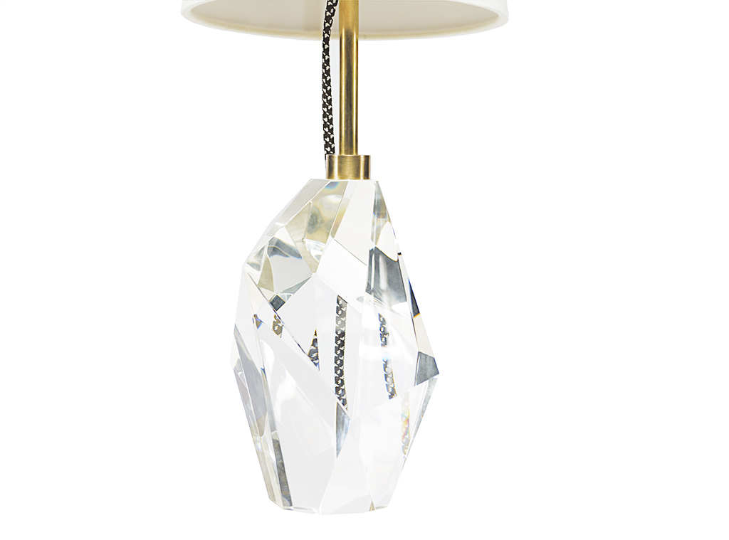 A clear crystal chandelier hanging from a ceiling with a gold base and a beige lampshade.