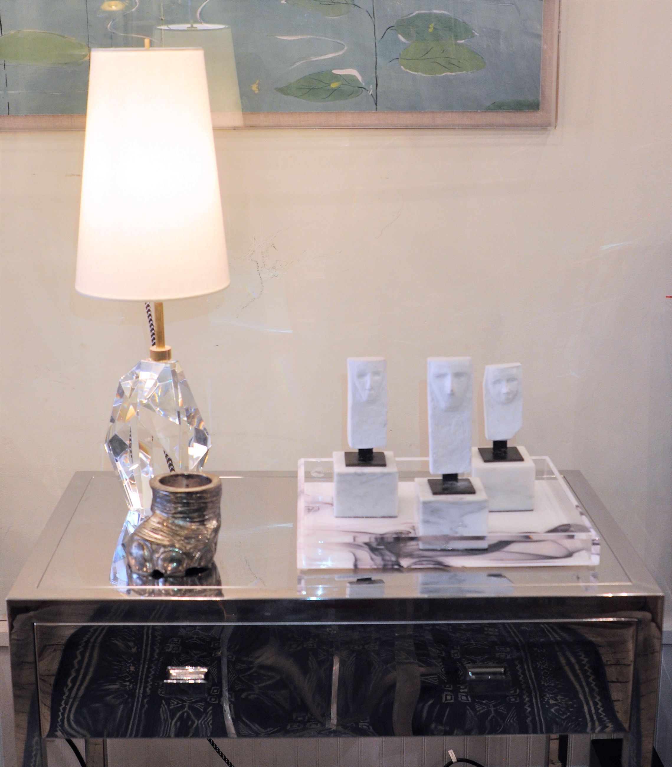 Kelly Wearstler Halcyon table lamp with a clear crystal base and a white linen shade on a glass top table accompanied by