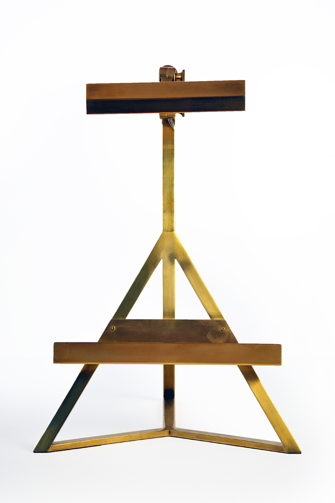 A brass tripod table lamp with a gold finish, standing on a white surface.