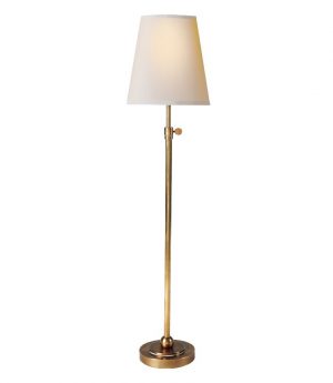 A tall table lamp with a white linen shade and a brass base, set against a neutral background.