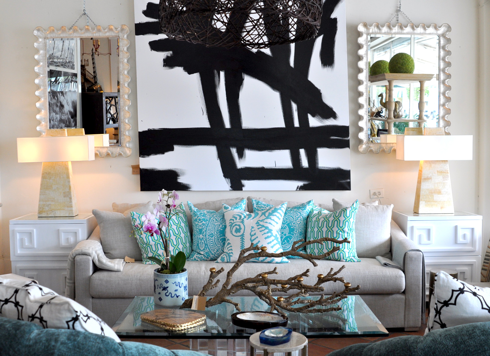 A modern faux bone obelisk table lamp with a rectangular shade set against a backdrop featuring a large abstract painting and a