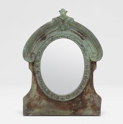 The image displays a large, oval-shaped mirror with an intricate design and a verdigris finish. It is set against a plain background.