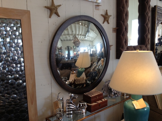 A large, round convex mirror with an antique brass frame, reflecting a room with a starfish decoration and a lamp.