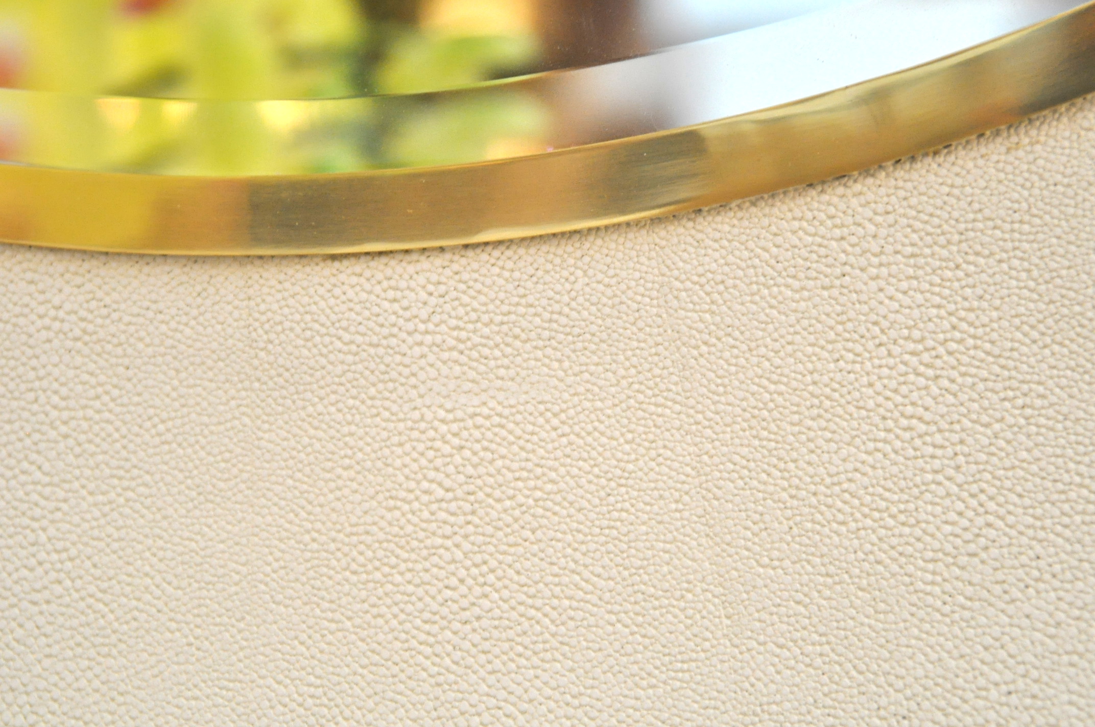 A round mirror with a beveled edge, featuring a snow faux shagreen design and trimmed in brass or silver.