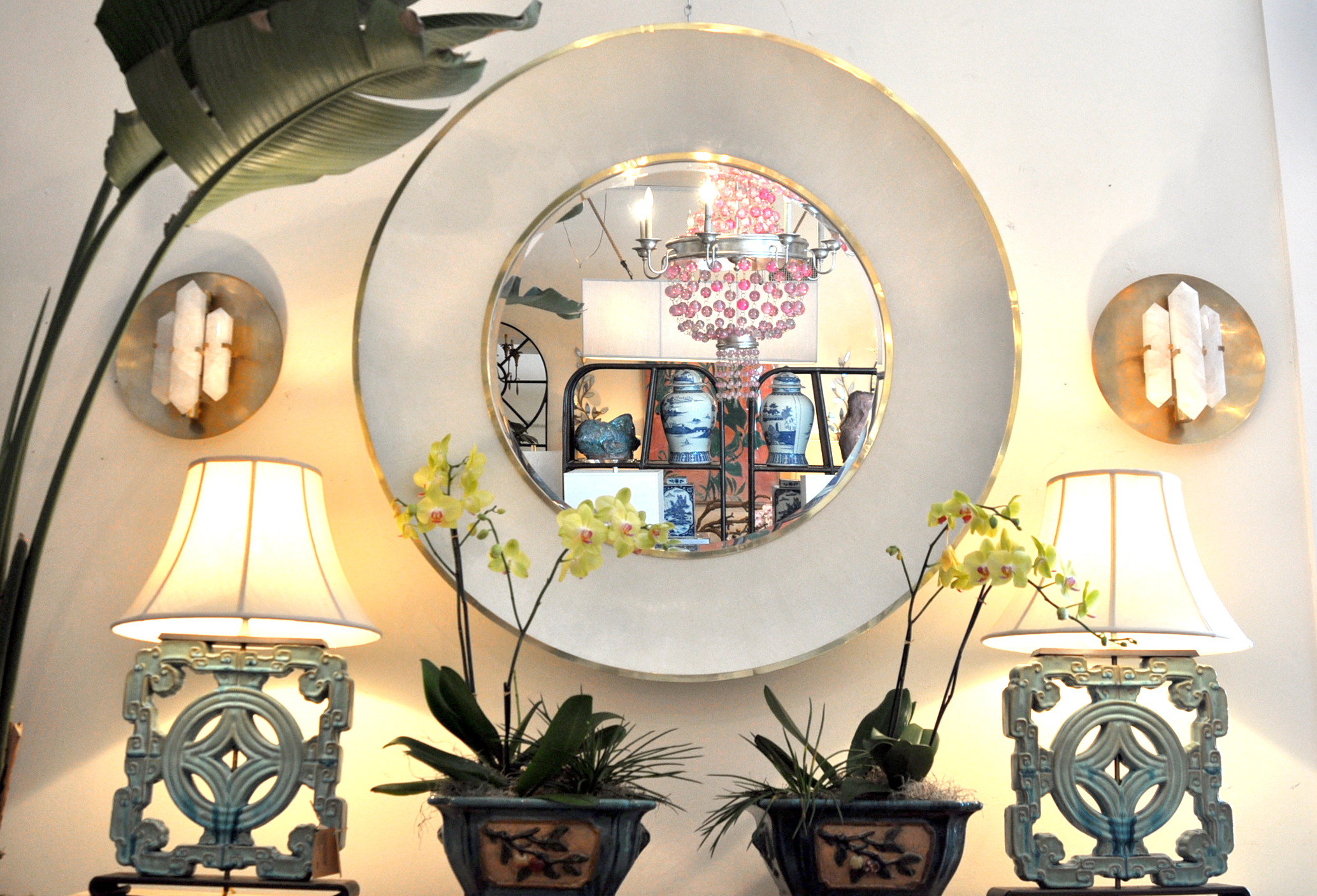Round mirror with a silver frame, reflecting a room with potted plants and decorative items.