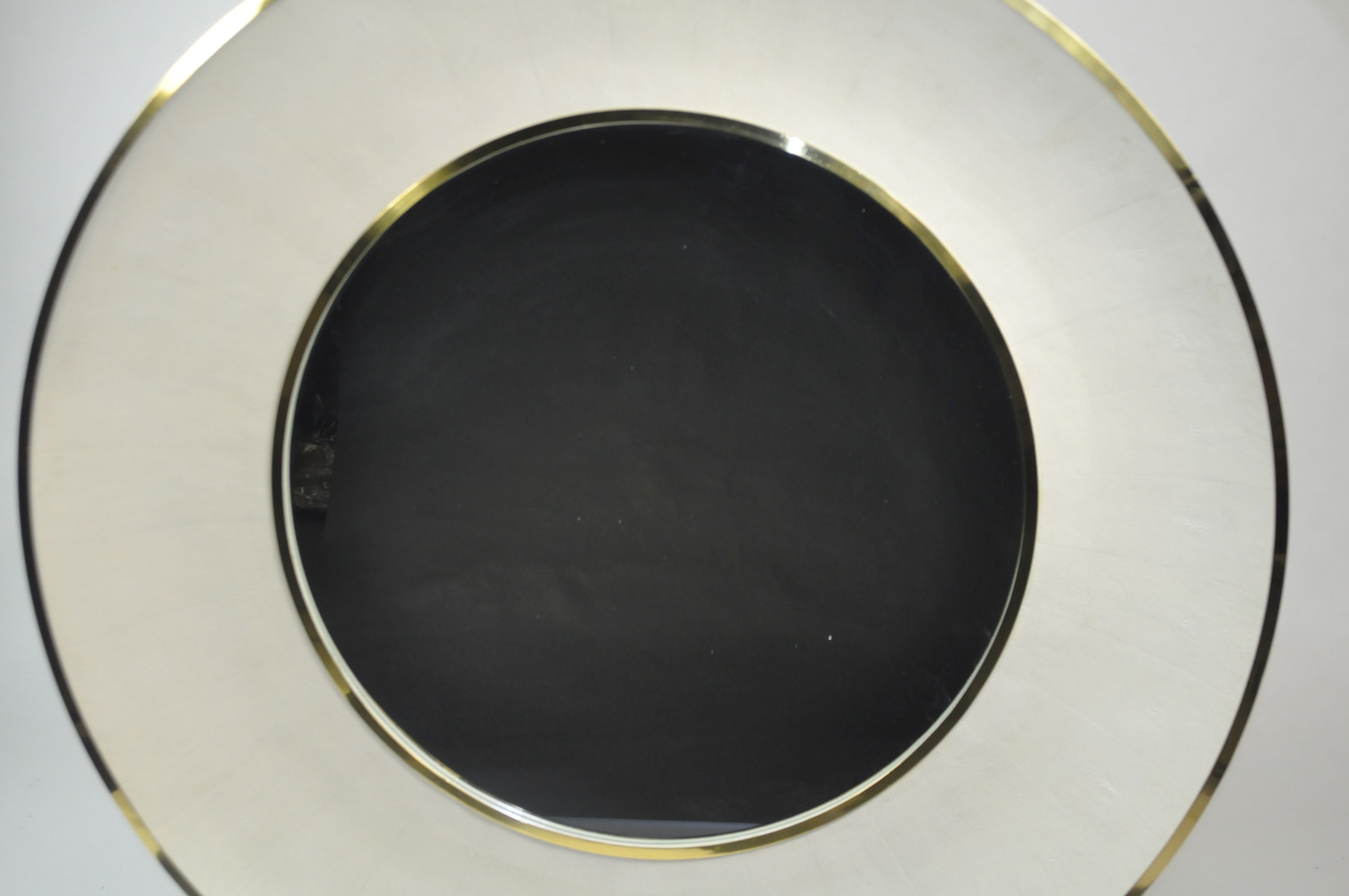Round mirror with a black center and gold trim, set against a white background.