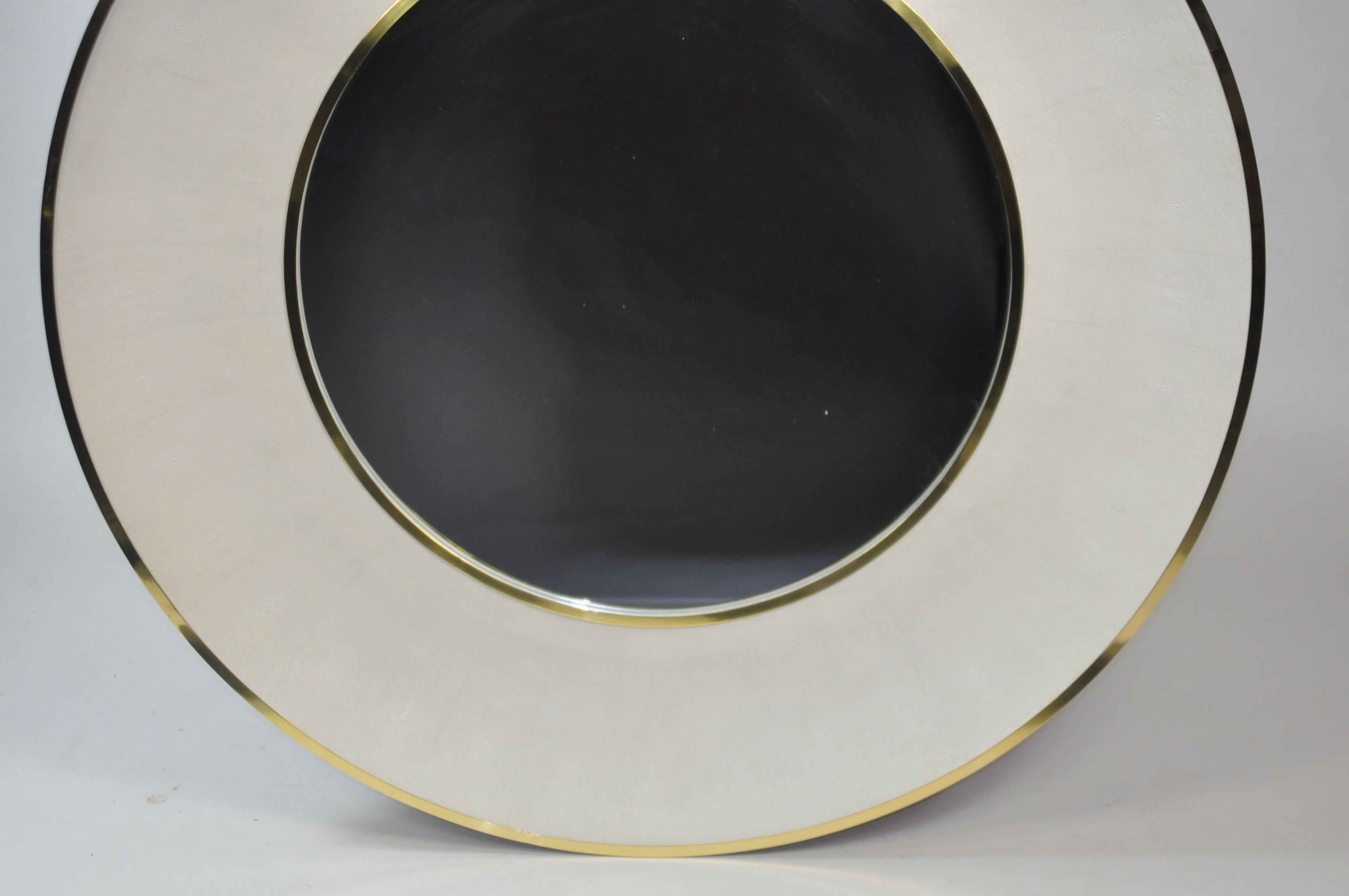 A round mirror with a beveled edge and a faux shagreen finish, available in silver or brass trim.