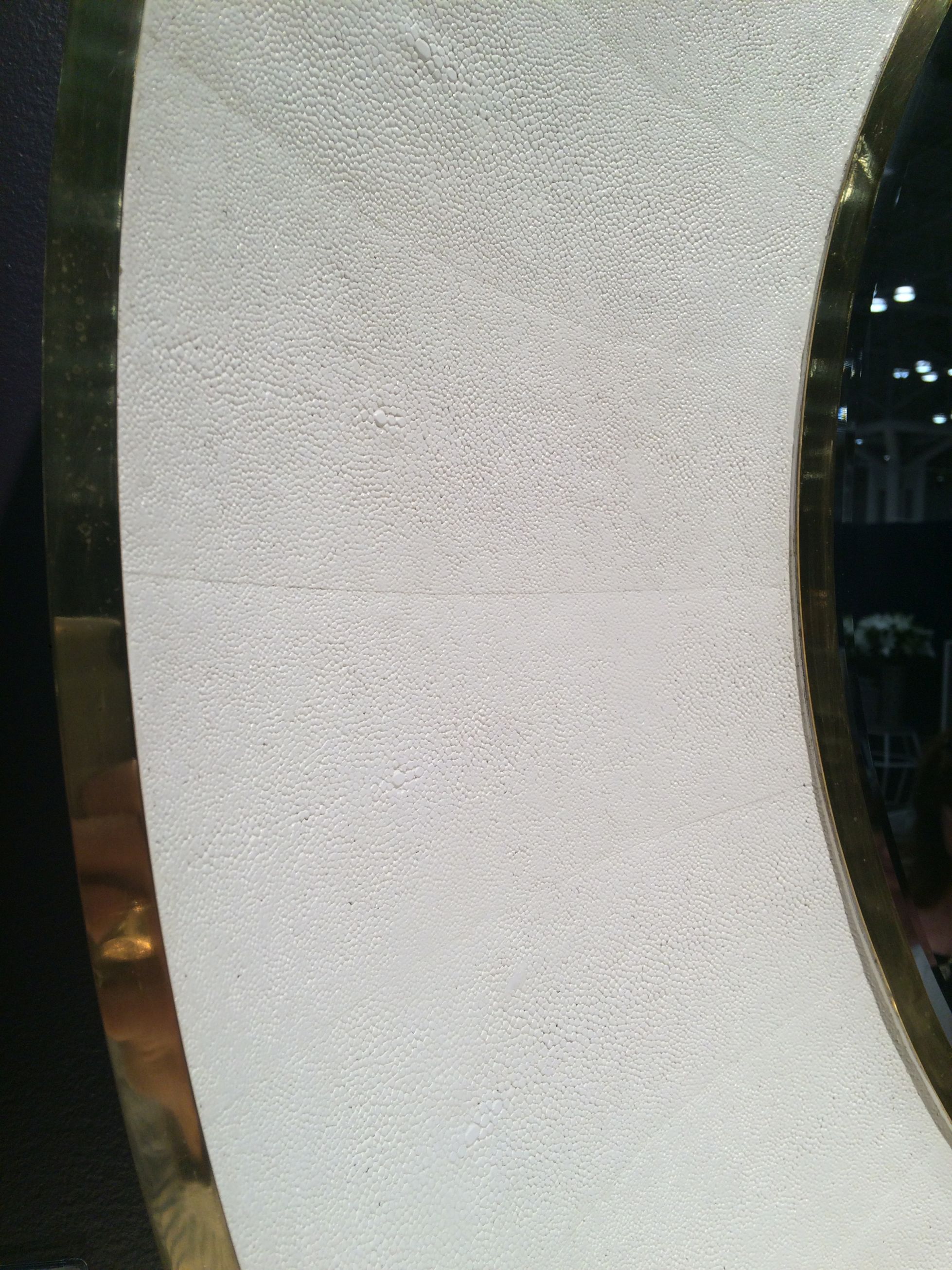 A round mirror with a beveled frame, featuring a snow faux shagreen design and available in silver or brass trim.