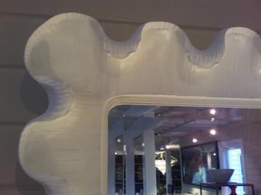 The image displays a large curved antiqued white resin mirror with a wavy design It is mounted on a wall and has