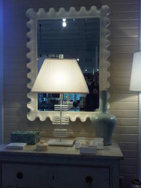 Antiqued white resin wave mirror with a bevel frame placed on a wall in front of a lamp and a small table