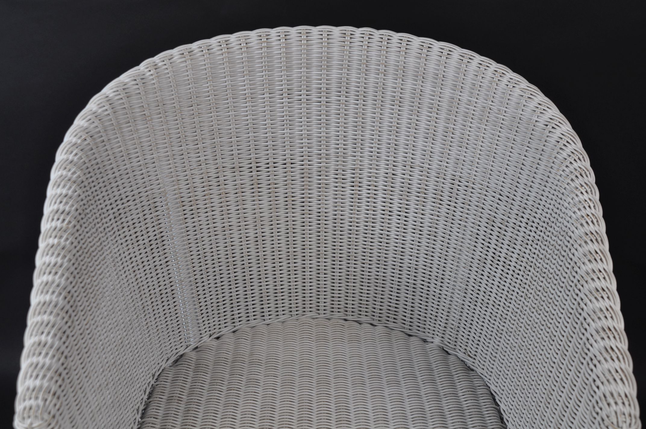 White and grey wicker armchair with a rounded backrest, set against a dark background.