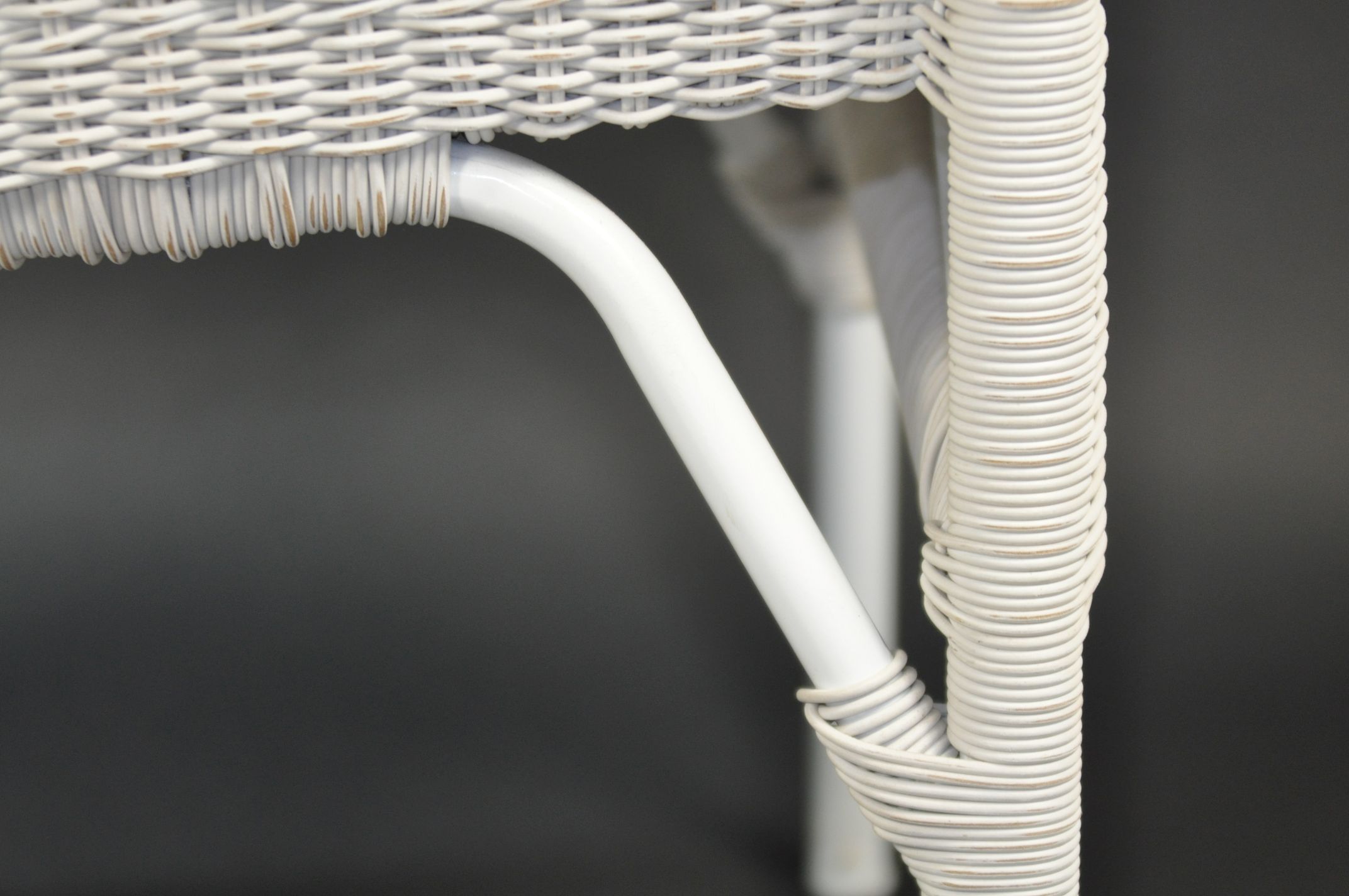 A wicker arm chair with a curved backrest available in white or grey finish showcasing its design and texture from an overhead