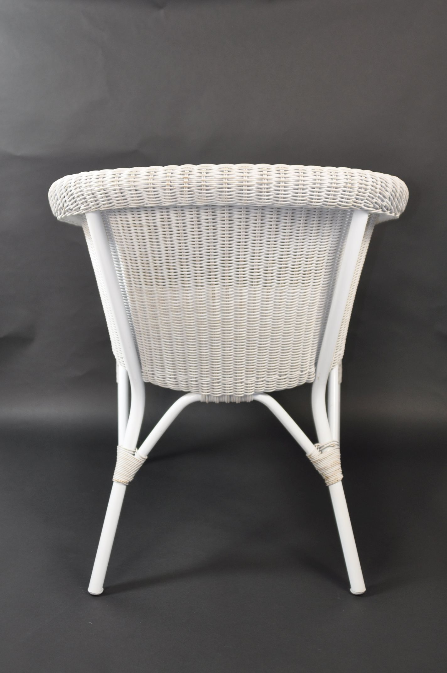 White wicker armchair with a curved backrest, placed against a dark background.
