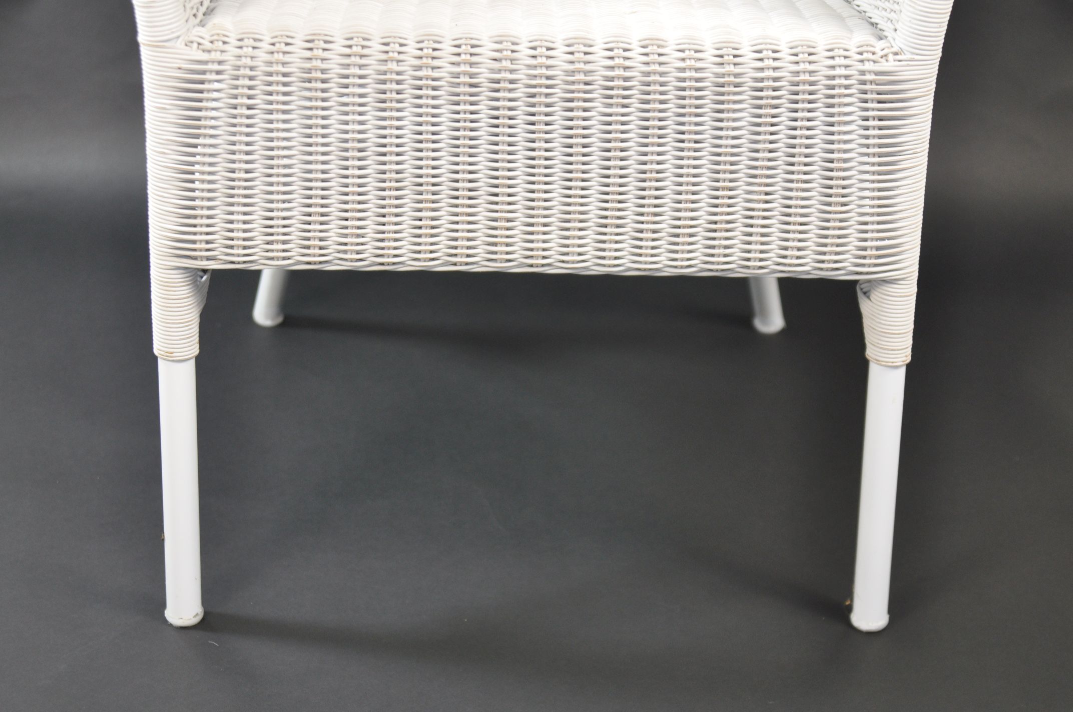 Wicker outdoor armchair with white frame and cushioning, positioned against a dark background.