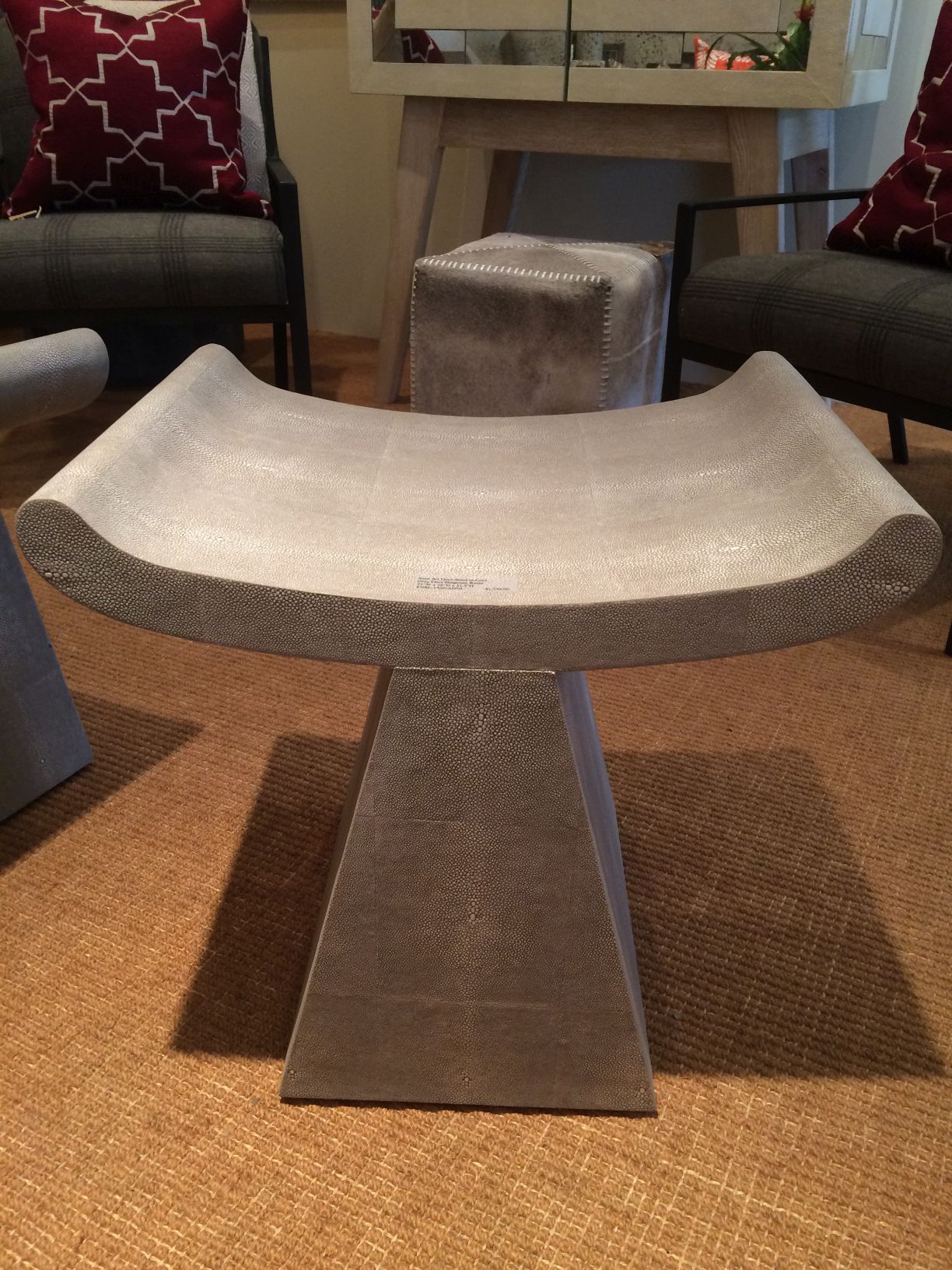 A modern, rectangular stool with a grey faux shagreen top and a dark grey base, standing on a beige carpeted floor.