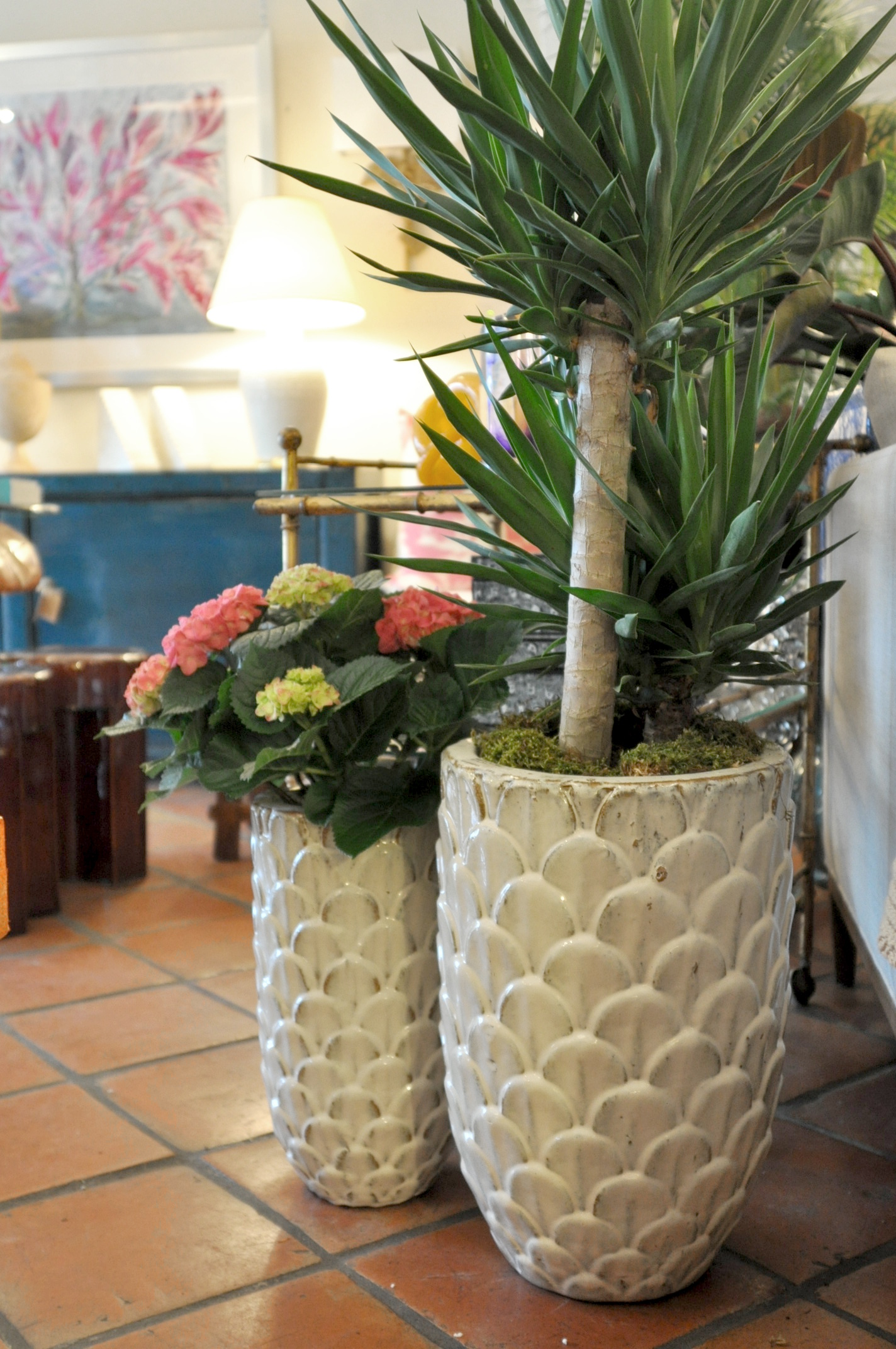 Three white pine cone planters on a tiled floor, each containing a small plant and flowers.